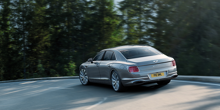 Bentley Hatfield Bentley Flying Spur Speed sedan side profile in Tourmaline Green paint driving dynamically on a mountain road at sunset